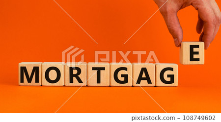'Mortgage' written on wood blocks. Male hand. Business concept. Copy space. Beautiful orange background. 'Mortgage' written on wood blocks. Male hand. Business concept. Copy space. Beautiful orange background. 108749602