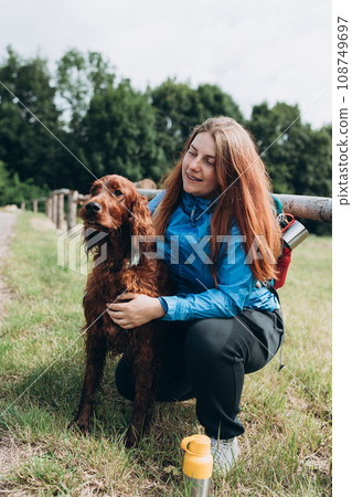 Happy 30s Girl loving and hugging tightly her dog. Travel and hiking with pet. Redhead Woman in active trekking clothes with dog having a halt after hiking, irish setter 108749697
