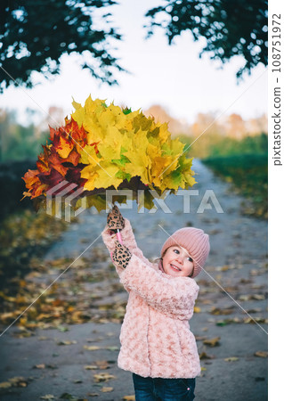Autumn portrait of little girl holding beautiful umbrella covered with yellow maple leaves 108751972