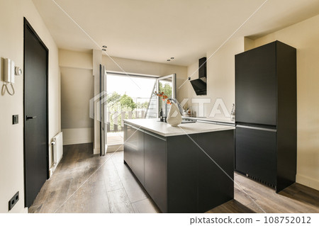 a kitchen with wood flooring and black cabinetd cupboards on the wall behind it is a large open door that leads to an outdoor patio 108752012