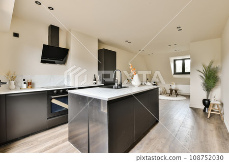 a modern kitchen with black cabinets and white marble countertops in the room is very light colored wood flooring 108752030