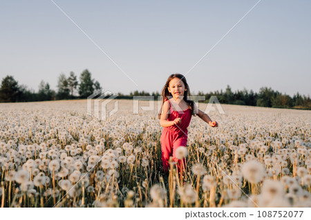 Energetic kid running in field full of white dandelions. Happy girl enjoying nature at sunset in meadow of blowballs. 108752077