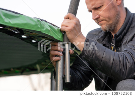 Serious man connecting details of frame for trampoline net with hands and furrowing eyebrows collecting equipment . Serious man connecting details of frame for trampoline net with hands and furrowing eyebrows collecting equipment . 108752108