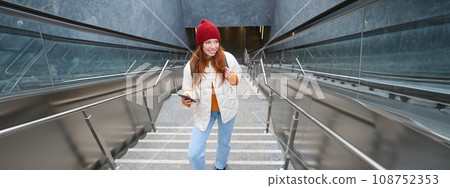 Outdoor shot of young woman plans route, follows map on smartphone app, goes up stairs with backpack and smiles Outdoor shot of young woman plans route, follows map on smartphone app, goes up stairs with backpack and smiles 108752353