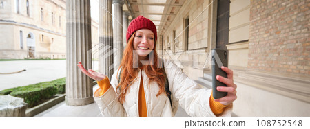 Happy girl tourist demonstrates something on video chat smartphone, shows sightseeing attraction to friend while on mobile phone app call 108752548
