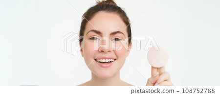 Wellbeing and skin care concept. Beauty woman shows cotton pad after washing her face with cleanser, using toner to take off makeup, standing over white background Wellbeing and skin care concept. Beauty woman shows cotton pad after washing her face with cleanser, using toner to take off makeup, standing over white background 108752788