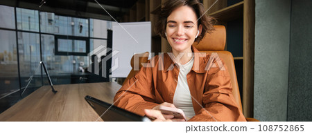 Young woman working in office, sitting with digital tablet, waiting for a meeting in conference room Young woman working in office, sitting with digital tablet, waiting for a meeting in conference room 108752865