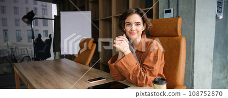 Image of young office worker, employee in casual clothes, businesswoman sitting at her desk and smiling Image of young office worker, employee in casual clothes, businesswoman sitting at her desk and smiling 108752870