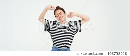 Portrait of woman feeling pleased after good nap, stretching arms and smiling, standing over white background Portrait of woman feeling pleased after good nap, stretching arms and smiling, standing over white background 108752938