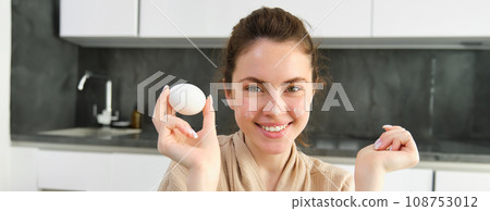 Attractive young cheerful girl baking at the kitchen, making dough, holding recipe book, having ideas 108753012