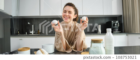 Attractive young cheerful girl baking at the kitchen, making dough, holding recipe book, having ideas 108753021