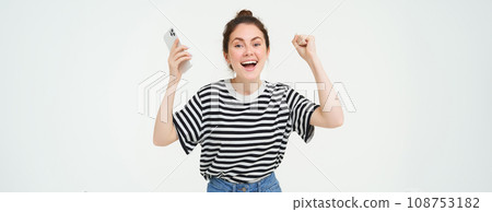 Portrait of happy woman laughing, holding telephone, using smartphone and chanting, rooting for someone, holding hands up, isolated over white background Portrait of happy woman laughing, holding telephone, using smartphone and chanting, rooting for someone, holding hands up, isolated over white background 108753182