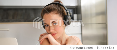 Close up portrait of fitness woman, wearing sportsbra, listening music in headphones, working out at home, doing exercises for fit and healthy body Close up portrait of fitness woman, wearing sportsbra, listening music in headphones, working out at home, doing exercises for fit and healthy body 108753183