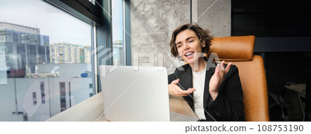 Portrait of young businesswoman, saleswoman giving speech online, talking to laptop while sitting in office, making presentation, having discussion with coworkers, meeting on remote Portrait of young businesswoman, saleswoman giving speech online, talking to laptop while sitting in office, making presentation, having discussion with coworkers, meeting on remote 108753190