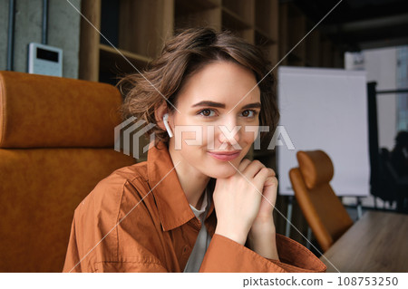 Close up portrait of smiling young woman, office employee sitting in conference room, looking happy at camera Close up portrait of smiling young woman, office employee sitting in conference room, looking happy at camera 108753250