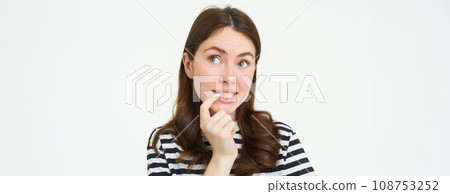 Portrait of curious young woman, bites her finger and looks up thoughtful, thinking, makes decision, choosing smth to eat, stands over white background Portrait of curious young woman, bites her finger and looks up thoughtful, thinking, makes decision, choosing smth to eat, stands over white background 108753252