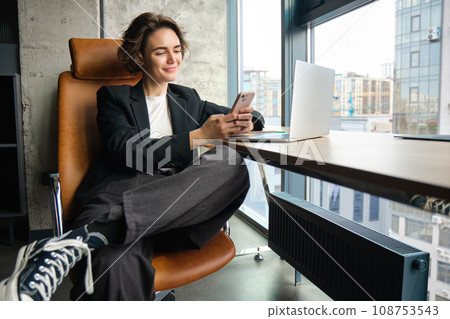 Portrait of stylish businesswoman working in office, using empty coworking room, sitting with laptop and smartphone 108753543
