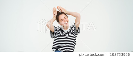 Portrait of cute caucasian woman, makes animal ears, cute pose, smiling at camera, standing over white background 108753966