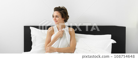 Image of young brunette woman with messy hair, waking up in her bed, sitting and looking aside with sensual, sleepy smile, cover herself with linen white sheets Image of young brunette woman with messy hair, waking up in her bed, sitting and looking aside with sensual, sleepy smile, cover herself with linen white sheets 108754648