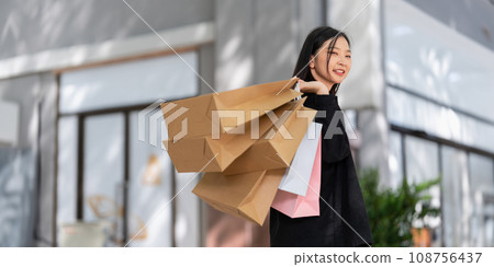 Young asian woman in shopping. Fashion woman in black with shopping bag walking around the city after shopping. Black friday Young asian woman in shopping. Fashion woman in black with shopping bag walking around the city after shopping. Black friday 108756437