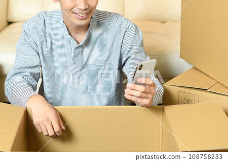 Young Asian man holding a smartphone in front of cardboard Young Asian man holding a smartphone in front of cardboard 108758283