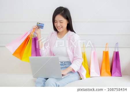 Young asian woman sitting on sofa using laptop computer shopping online with credit card. 108758434