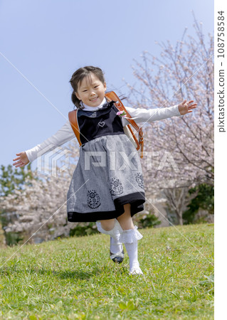 背著書包的一年級學生走過櫻花盛開的公園 108758584