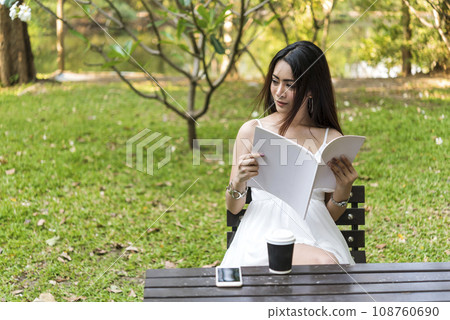 Asian woman holding book reading magazine at green park in natural garden. Young woman relaxation read open book self study. University women smiling with happiness learning. Women sit in green park Asian woman holding book reading magazine at green park in natural garden. Young woman relaxation read open book self study. University women smiling with happiness learning. Women sit in green park 108760690
