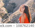 Young attractive brunette woman sitting on the background of the mountains, enjoying the sunshine. Concept of traveling, hiking, vacation and leisure 108762140