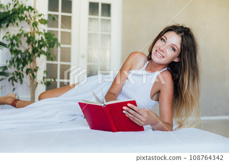 Beautiful slender woman in pajamas reading a book in the bedroom on the bed 108764342