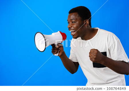 Positive african guy shouting with megaphone over blue background 108764849