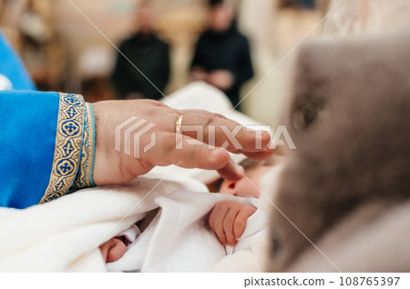 The priest performs the rite of baptism of the child and anoints the leg with holy peace. 108765397