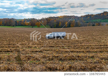 White agricultural truck in a harvested corn field autumn colors trees White agricultural truck in a harvested corn field autumn colors trees 108765443