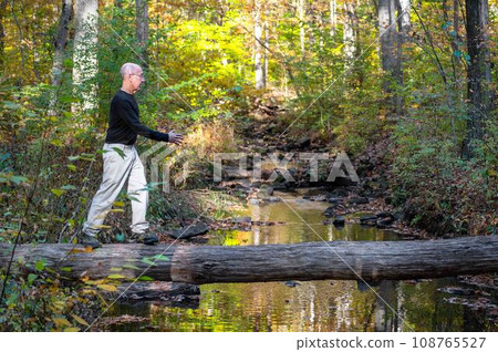 Active fit senior man hikes over fallen log foot bridge autumn woods 108765527