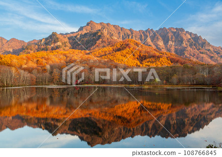 Togakushi mountain range with autumn leaves bathed in the morning sun reflected in Kagami Pond Togakushi mountain range with autumn leaves bathed in the morning sun reflected in Kagami Pond 108766845