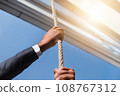 Businessman holding a rope hanging from a building 108767312