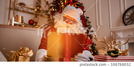 Surprised Santa Claus with glowing gift near christmas tree. New year and Merry Christmas concept 108768032
