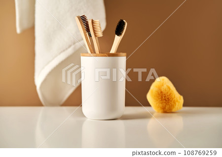 Bamboo toothbrushes in a cup and a towel in a bathroom interior. 108769259