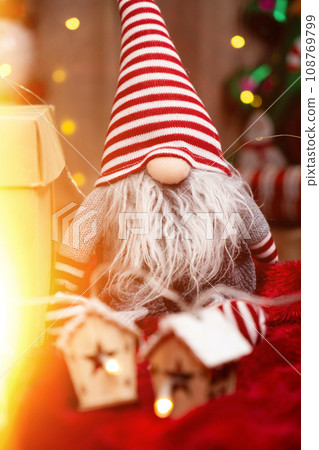 Christmas toy gnome with a striped cap on his head and glowing garlands. 108769799