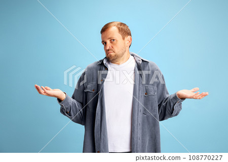 I don't know. Confused handsome young man standing and shrugs his shoulders, throws up his hands isolated blue studio background. Concept of studying. 108770227