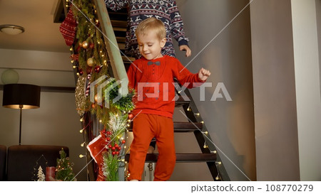 Happy cheerful family running down the stairs on Christmas morning to open gifts and presents from Santa. Family celebrations on winter holidays. Happy cheerful family running down the stairs on Christmas morning to open gifts and presents from Santa. Family celebrations on winter holidays. 108770279
