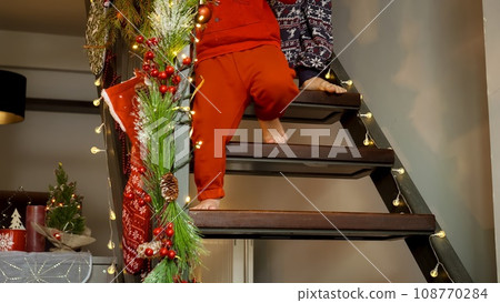 Closeup of children's feet walking down the wooden stairs decorated for Christmas at morning. Family celebrations on winter holidays. Closeup of children's feet walking down the wooden stairs decorated for Christmas at morning. Family celebrations on winter holidays. 108770284
