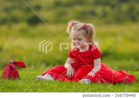 little girl in a red dress sitting on the lawn 108770440
