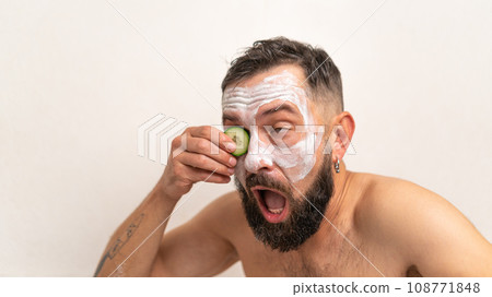 Funny man with cucumber and beauty mask on face in bath at home Funny man with cucumber and beauty mask on face in bath at home 108771848