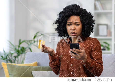 Upset unhappy and cheated woman sitting at home on sofa in living room, displeased rejected online money transfer error, holding bank credit card and phone. Upset unhappy and cheated woman sitting at home on sofa in living room, displeased rejected online money transfer error, holding bank credit card and phone. 108772024