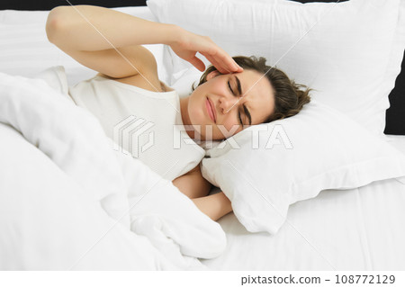 Woman feeling unwell, lying in bed, touching head and frowning, has headache, severe migraine Woman feeling unwell, lying in bed, touching head and frowning, has headache, severe migraine 108772129