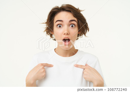 Close up portrait of girl with surprised face, points at herself, looks shocked, stands over white background Close up portrait of girl with surprised face, points at herself, looks shocked, stands over white background 108772240