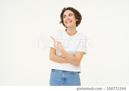 Portrait of brunette girl showing banner, pointing finger left, advertising, standing over white background 108772264