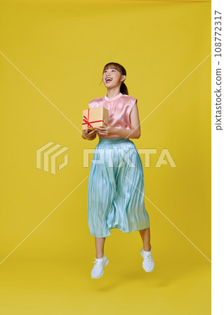 Full size profile photo of pretty  lady jump with present isolated on yellow background 108772317
