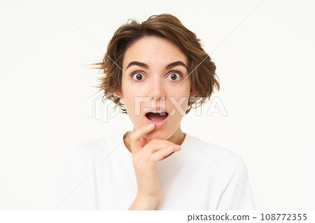 Close up of amused, intrigued young woman, drops jaw and listens with interest, stands over white background 108772355